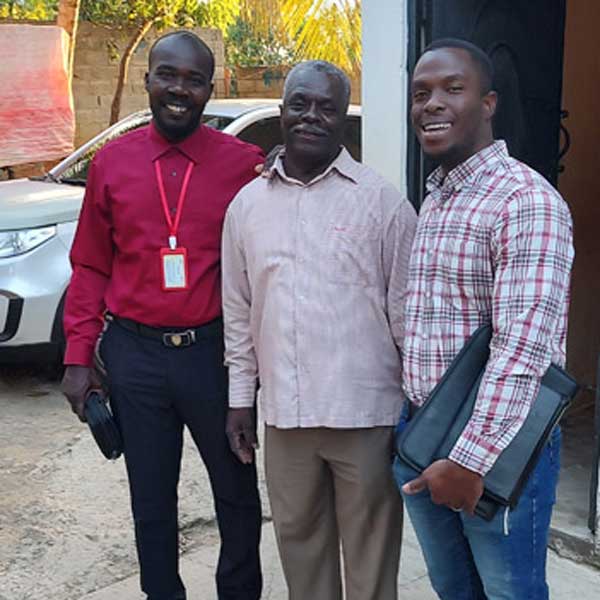 Three men from Haiti standing in front of a car, reflecting the challenges faced by people living with poverty.